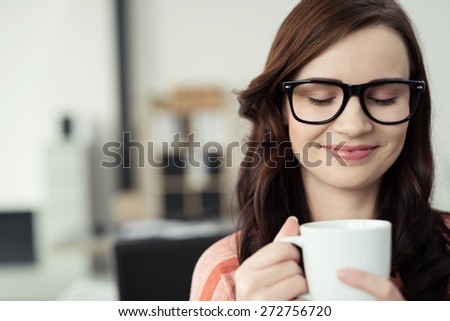 Close Up of Young Brunette Woman Wearing Eyeglasses with Black Frames Holding Mug Containing Warm Beverage and Inhaling Comforting Warm Scent