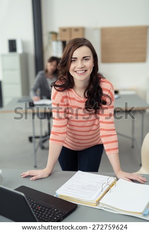 Close up Smiling Young Pretty Woman in Stripe Long Sleeves Shirt Leaning on the Table with Notes and Laptop While Looking at the Camera.