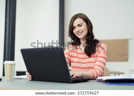 Happy Attractive Young Woman Sitting at the Table with Documents and a Cup of Coffee on Top While Using her Laptop Computer.