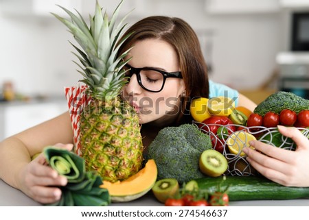 Young Woman Wearing Eyeglasses with Black Frames Embracing Variety of Fruits and Vegetables and Kissing a Pineapple