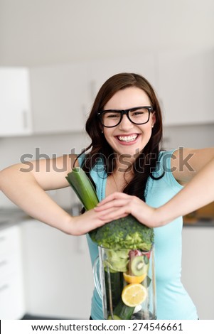 Close up Smiling Pretty Girl Pushing Large Veggies on a Kitchen Blender Device While Looking at the Camera.