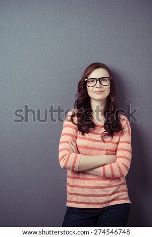 Confident young woman wearing glasses standing with folded arms leaning against a dark background smiling at the camera