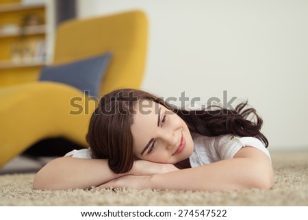 Happy woman lying on the carpet daydreaming with her head resting on her folded arms and a smile of pleasure on her face