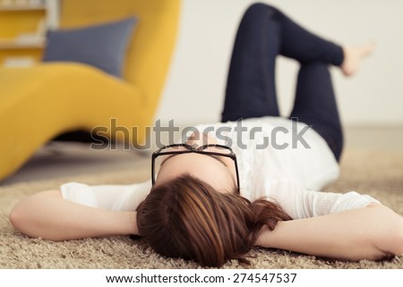 Young Woman Wearing Eyeglasses Relaxing on the Floor with Carpet with Hands at the Back her Head and Knees Bent