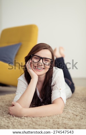 Happy Attractive Young Woman Lying on her Stomach on the Floor with Carpet While Leaning on her Arm and Looking at the Camera.