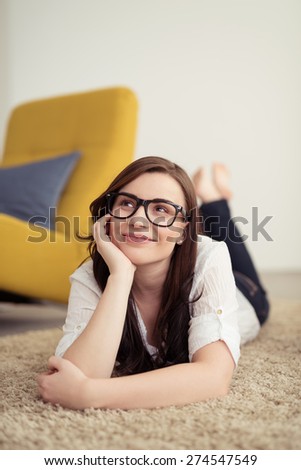 Happy Thoughtful Pretty Young Girl with Eyeglasses Lying on her Stomach on the Floor While Leaning on her Arm and Looking Up.