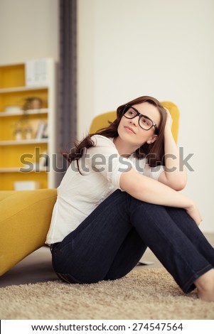 Thoughtful Pretty Girl with Glasses Leaning on her Knees While Sitting on the Floor and Looking to the Upper Left of the Frame.