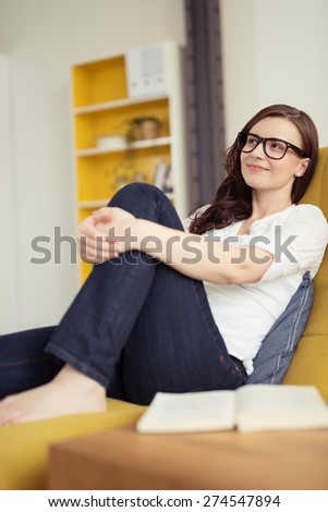 Pretty Young Woman Leaning her Back on Sofa While Embracing her Knee and Looking Upper Left of the Frame.