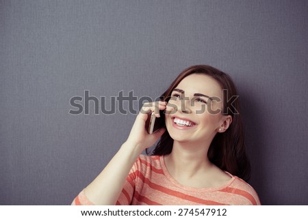 Close up Happy Young Woman Talking to Someone on Mobile Phone While Looking Up on a Gray Wall Background with Copy Space.
