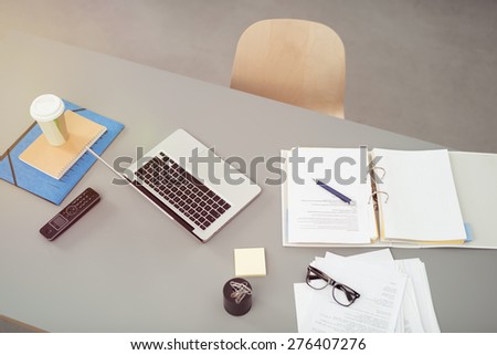 Overhead view of an office workstation with open notebooks, a laptop computer notes, eyeglasses and a vacant chair