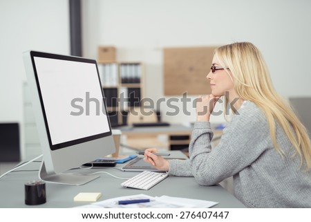 Young businesswoman wearing glasses sitting at her desk reading her blank white computer screen, profile view in the office