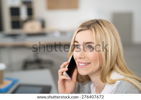 Young woman smiling as she chats on her mobile phone listening to the conversation and staring thoughtfully into the distance