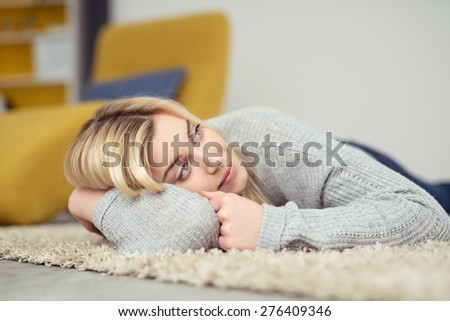 Close up Thoughtful Blond Girl Lying on the Carpeted Floor at the Living Room, Leaning on her Arm and Looking Up