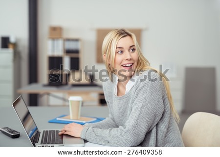 Attractive casual young woman turning with a smile to look at a colleague in the office a she sits at her desk, natural expression