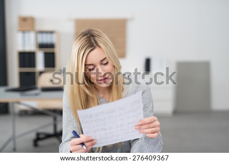 Young office worker checking a document holding it in her hands reading through the text with a pen in her hands