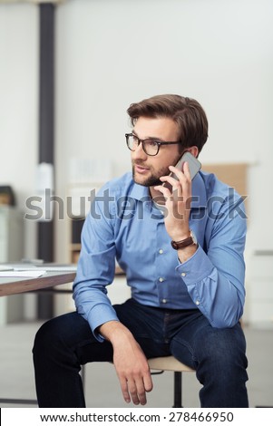 Handsome Young Businessman Sitting on a Chair and Leaning on his Knees While Talking to Someone on Mobile Phone.