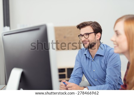 Two young people working in the office with a view past the face of a smiling woman to a businessman working at his desktop computer