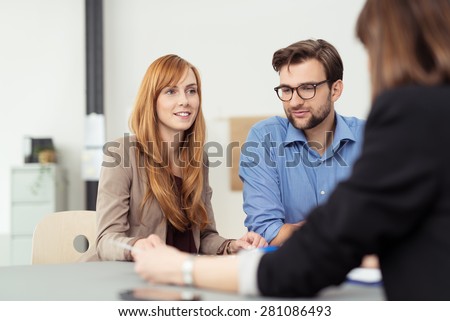Young married couple in a meeting with a broker or agent with focus to the attractive redhead wife