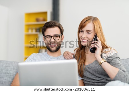 Smiling Couple Sitting on Sofa with Laptop Computer and Cordless Telephone, Placing an Order or Shopping Online