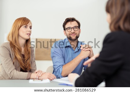 Broker having a discussion with a young couple who are sitting listening to her with serious attentive expressions