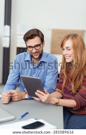 Successful young businessman and woman smiling as they sit together at a table in the office using a tablet computer for their work