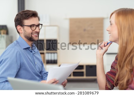 Happy co-workers at the office discussing paperwork together looking at each other with friendly smiles, man and woman