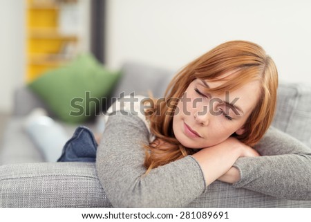 Tired attractive redhead woman taking a nap as she lies stretched out on her stomach on a sofa, close up of her face