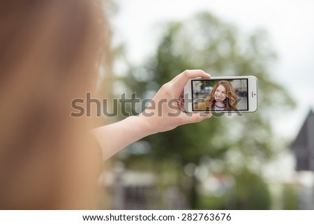 Hand of a Blond Girl Holding her Mobile Phone in Horizontal Orientation While Taking Selfie Photo at the Street.