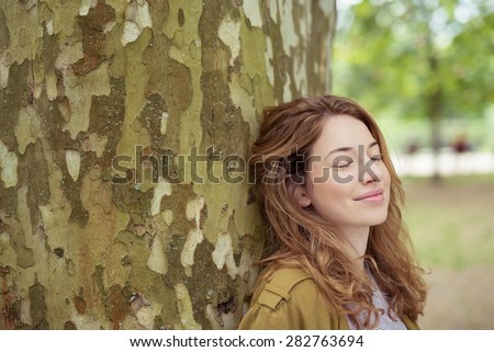 Close up Thoughtful Pretty Blond Teen Girl Leaning her Back Against Huge Tree Trunk with Eyes Closed and Smiling Face.