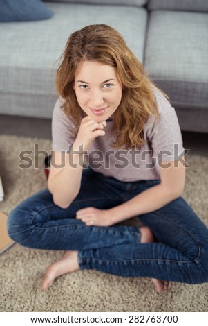 Portrait of Young Brunette Woman Dressed in Jeans and T-Shirt Sitting Cross Legged on Carpeted Floor of Living Room at Home