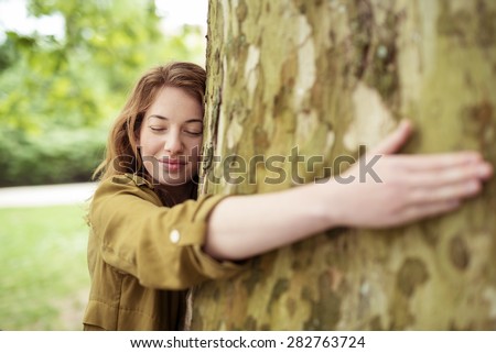 Thoughtful Blond Teen Girl Hugging Huge Tree Trunk at the Park with Eyes Closed and Smiling Face.