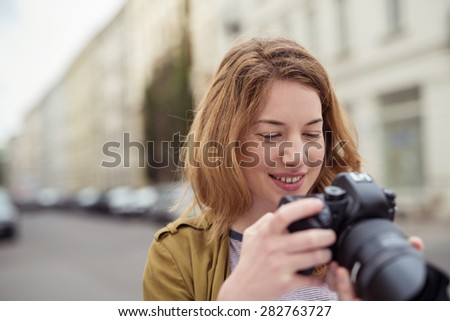 Close Up of Smiling Young Woman Looking at Rear Display of Digital SLR Camera Outdoors in Urban Setting