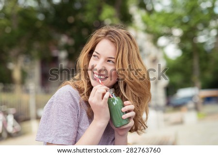 Close up Cheerful Blond Teen Girl Holding a Bottle of Green Juice, Looking Up at her Back While Thinking of Something Good.