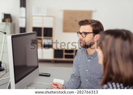 Two young employees, man and woman, staring at a turned off PC monitor while sitting at desk in the interior of an office with modern equipment