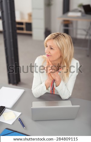 Thoughtful Blond Adult Businesswoman Leaning on her Elbow While Sitting at the Table with Laptop and Looking Into Distance.