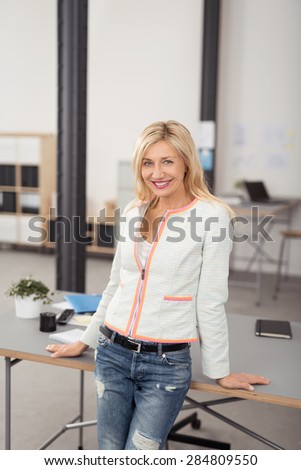 Happy Portrait of a Blond Office Woman Leaning her Back Against her Desk While Looking at the Camera.