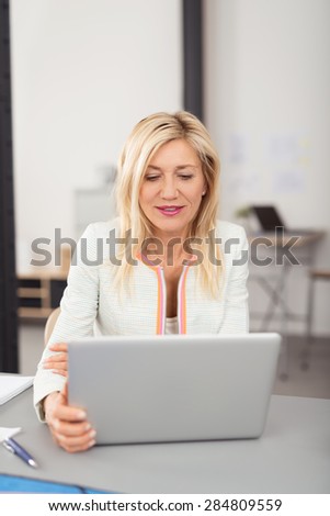 Attractive stylish middle-aged blond businesswoman working on a laptop computer reading information on the screen with a serious expression