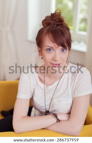 Close up Pretty Young Woman in Casual Wear, Sitting on a Yellow Chair with Arms Crossed and Smiling at the Camera.