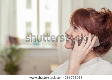Close up profile view of a pretty young redhead woman chatting on her mobile smiling happily as she listens to the conversation