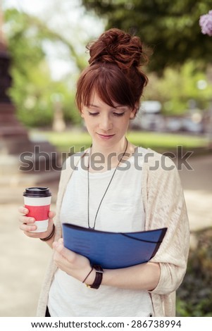 Close up Attractive Girl Student Holding a Cup of Coffee While Reading Something on Top of the File Folder on her Other Hand.