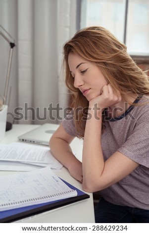 Pretty Blond Teen Girl Sitting at her Study Room, Reading her Lessons on her Notebook While Leaning on her Elbow on the Table.