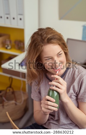 Young woman sitting enjoying a healthy broccoli smoothie from a glass bottle looking to the right of the frame with a happy smile
