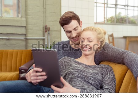 Happy Young Sweet Couple in Gray Shirts Sitting on the Sofa at the Living Area with Tablet Computer.