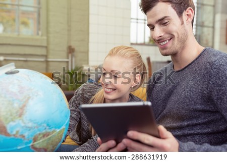 Close up Happy Young Couple Sitting at the Sofa with Tablet Computer In Front of a Table Globe