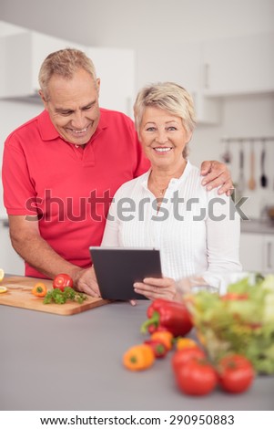Sweet Happy Senior Couple Using their Tablet Computer While Preparing Something to Eat for Dinner at the Kitchen