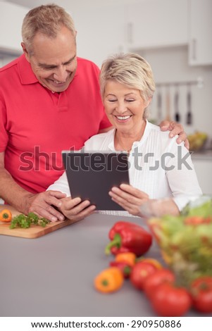 Happy Middle Aged Couple Watching Something on Tablet Computer While Preparing for Dinner at the Kitchen.