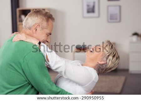 Happy Middle Aged Couple Dancing at the Living Room While Holding Each Other and Laughing.