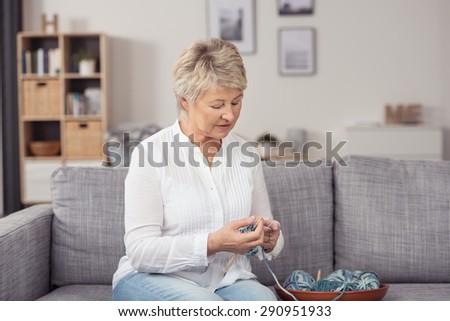 Middle Aged Woman in Casual Clothing, Sitting at the Living Room Couch and Knitting with Yarn Seriously