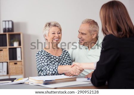 Happy Middle Aged Wife beside her Husband Shaking Hands to a Female Business Agent at the Table.