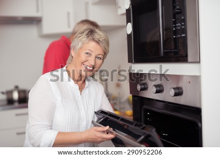 Happy Matured Woman Opening a Microwave Oven at the Kitchen While Looking at the Camera with a Toothy Smile.